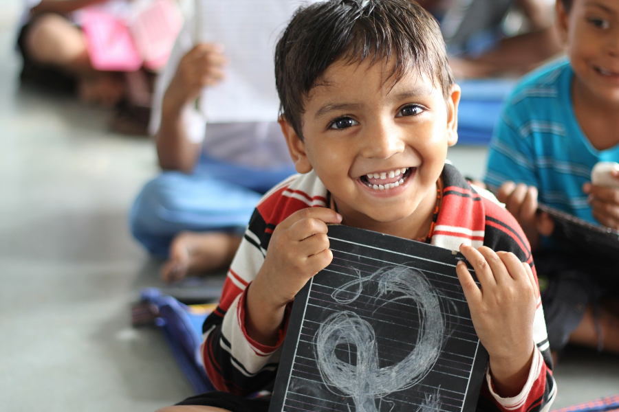 Niño sonriendo, abrazado con una pizarra pequeña