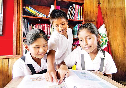 Dos niñas y un niño leyendo un libro, frente a una bandera de Perú