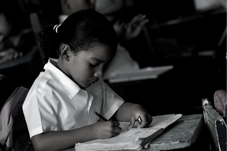 foto en negro y blanco de una niña escribiendo. Ella está de perfil