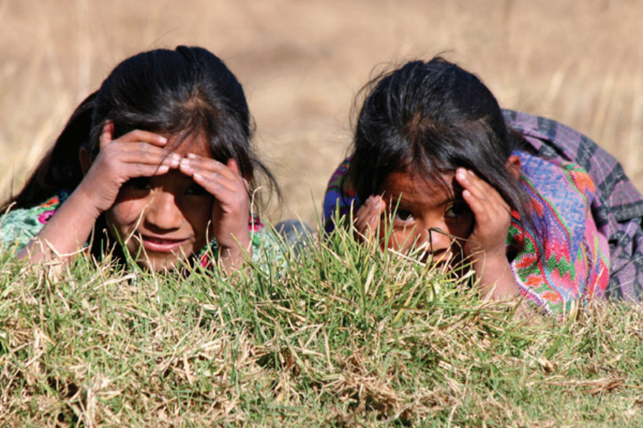 Dos muchachas acostadas boca abajo en la hierba, tapando los ojos con las manos