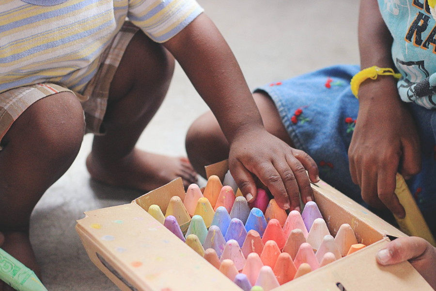 Dos niños pequeños en cuclillas junto a una caja de lápices de colores