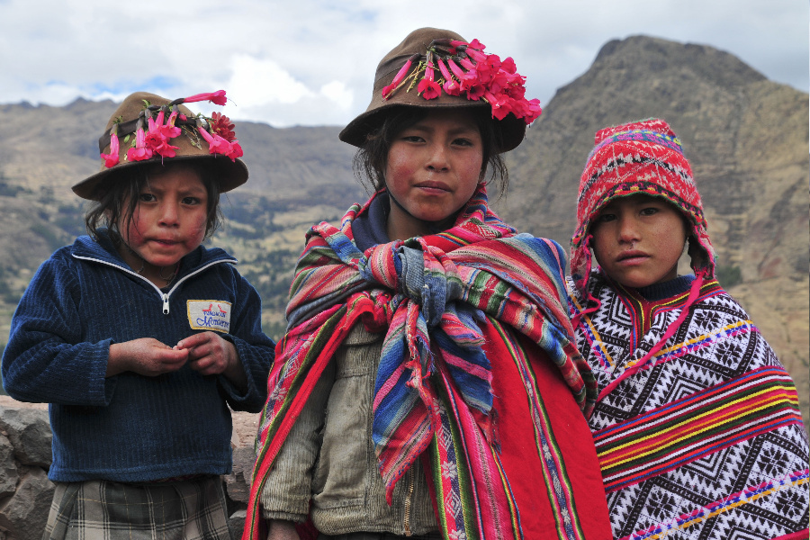Tres jóvenes peruanas vistiendo indumentaria tradicional. En la parte posterior de la imagen, hay montañas.