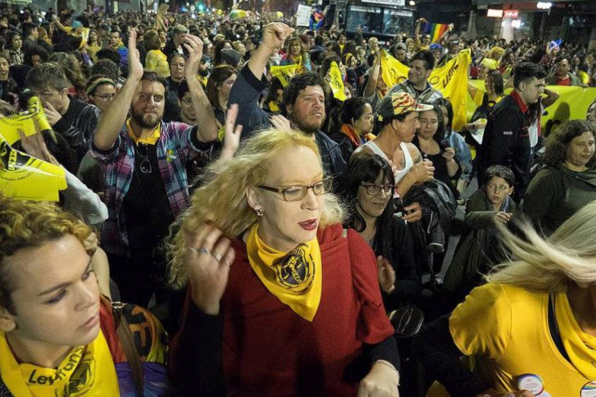 Mujeres trans protestando en la calle, usando un pañuelo amarillo alrededor del cuello